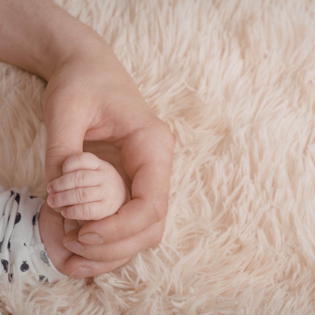 An adult hand gently holding a baby’s hand